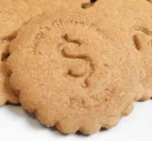 Image of a biscuit style cookie with serated edge. There is a depression the shape of a dollar symbol in the center.